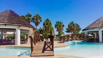 a resort swimming pool with a bridge and palm trees at Sandnblue - Encosta Do Lago Resort Club - Quinta do lago near Beach & lake BEST LOCATION in Quinta do Lago
