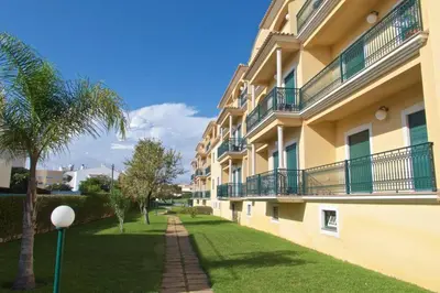 a building with a palm tree next to a yard at Albufeira Appartement avec piscine in Albufeira