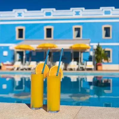 two glasses of orange juice next to a swimming pool at ADO HOUSE Albufeira in Albufeira