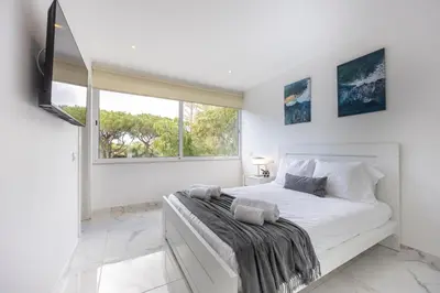 a white bedroom with a large bed and a window at Casa Verde Vilamoura in Quarteira
