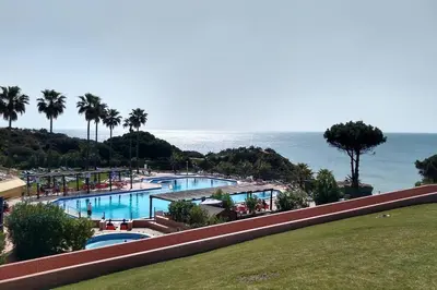 a large swimming pool with the ocean in the background at Beach Front Luxury T1 Apt Pools Garage Tennis in Albufeira