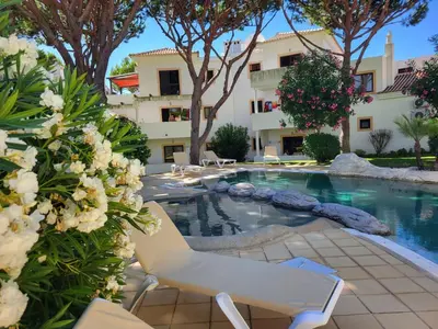 a swimming pool with two chairs and a building at T2 Falésia - Olhos de Água in Olhos de Água