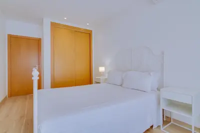 a white bedroom with a white bed and a wooden door at Side Villas - 1bdr Retreat with BBQ & Patio in Quarteira