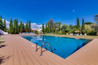 a large swimming pool with a wooden deck and trees at Side Villas - 1bdr Retreat with BBQ & Patio in Quarteira