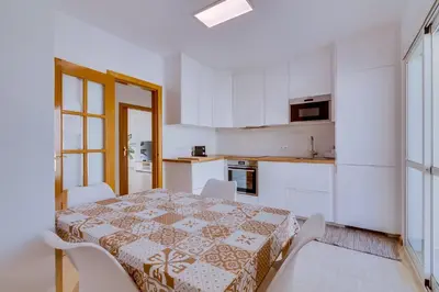 a white kitchen with a table and white chairs and a table and a table at Apartamento Al Sakia 2bdr com piscina e ar condicionado in Quarteira