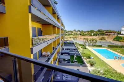 a yellow building with a swimming pool and a resort at Parque Atlântico Modern Seaview Apartment with Pool and Tennis Court in Cavacos