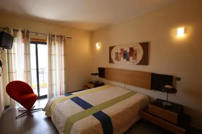 a bedroom with a bed and a red chair at Parque Atlântico Modern Seaview Apartment with Pool and Tennis Court in Cavacos