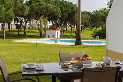 a table with a bowl of fruit on it with a pool at Stylish 2BR Ground Floor Apartment in Vila Sol, Direct Garden and Poolside Acces in Quarteira
