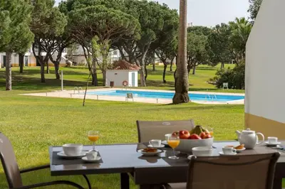 a table with a bowl of fruit on it with a view of a pool at Stylish 2BR Ground Floor Apartment in Vila Sol, Direct Garden and Poolside Acces in Quarteira