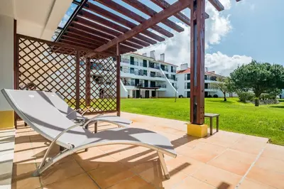 a white chair on a patio with a building in the background at Stylish 2BR Ground Floor Apartment in Vila Sol, Direct Garden and Poolside Acces in Quarteira
