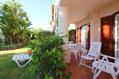 a patio with white chairs and a table and a bush at Old Village- 2A Village Street in Quarteira