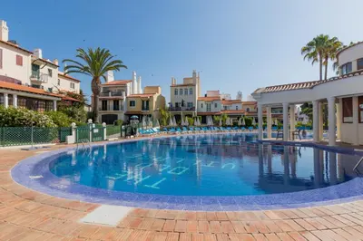 a large swimming pool with palm trees and buildings at Old Village- 1A Village Gate in Quarteira