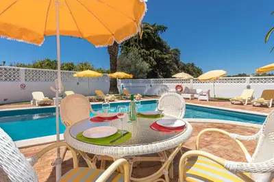 a table with chairs and an umbrella next to a pool at Albufeira Villa El-Gharb private 4 Bedrooms in Albufeira