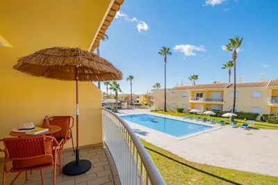 a balcony with a table and an umbrella and a swimming pool at Jardins Vale de Parra in Albufeira