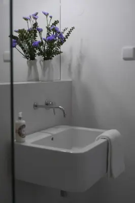 a white bathroom with a sink with flowers in a mirror at Casas Adentro in Faro