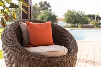 a wicker chair with an orange pillow sitting next to a pool at Quinta dos Figos - Jacuzzi Perto da Praia in Guia