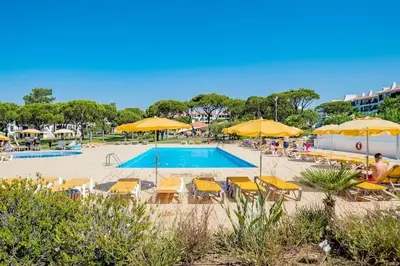 a pool with yellow umbrellas and chairs and people at 2 bedroom apt Vila Sol in Quarteira