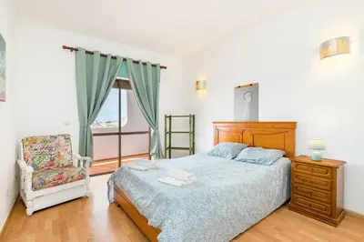 a bedroom with a bed and a chair and a window at TAC - Sunrise Montechoro Albufeira in Albufeira