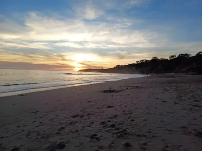 a beach with the sun setting on the ocean at Balaia Praia in Albufeira