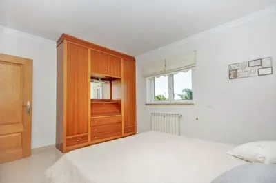 a white bedroom with a bed and a wooden cabinet at Quinta do Sol in Guia