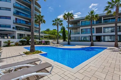 a swimming pool in front of a building with palm trees at Areias Branca in Quarteira