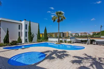 a swimming pool in a courtyard with a building and palm trees at Areias Branca in Quarteira