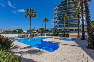 a swimming pool with palm trees and a building at Areias Branca in Quarteira