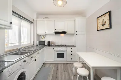 a kitchen with white cabinets and a sink and a table at Vilamoura Family Escape in Quarteira