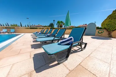 a row of lounge chairs next to a swimming pool at Stunning Villa with Heated Pool, Garden, BBQ in Quarteira