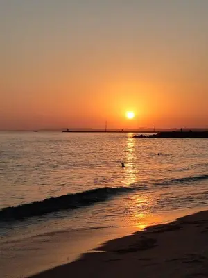 a sunset on the beach with the sun setting at Apartamento 5 min a pé da praia, com terraço ao sol, no 1º andar in Quarteira