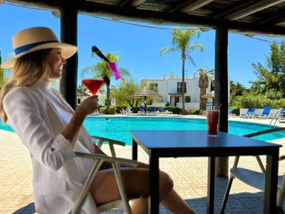 a woman in a hat sitting at a table with a drink at Ocean Vista Retreat with Beach & Pool Access by Drago Rentals in Albufeira