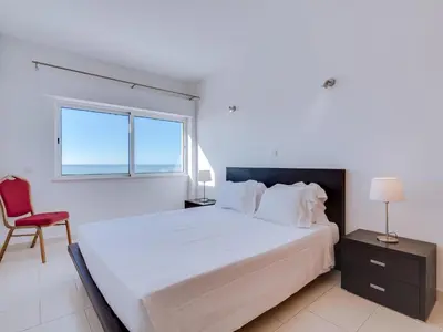 a bedroom with a large bed and a red chair at AL - Apartamento Canto do Mar frente à praia in Quarteira