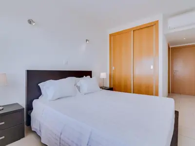 a bedroom with a large white bed and a wooden cabinet at AL - Apartamento Canto do Mar frente à praia in Quarteira