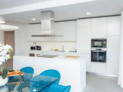 a white kitchen with blue chairs and a glass table at Green 3 Apartment by Stay ici Algarve Holiday Rental in Albufeira