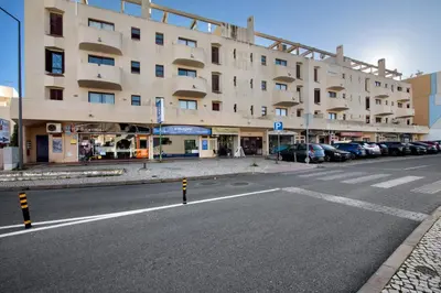 a large building with cars parked next to a street at Oura Beach Cozy Apartment in Albufeira