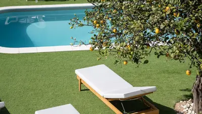 a white bench next to an orange tree next to a pool at Sunny 3BDR Apt with Pool in Ferreiras by LovelyStay in Albufeira