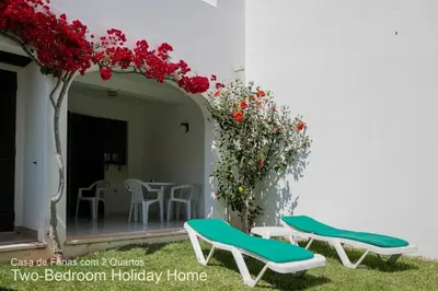 a patio with two chairs and a table with red flowers at Akivillas Quarteira Relax in Quarteira