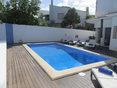 a large swimming pool on a deck with a white wall and chairs at Luxury Villa with Private pool walking distance to beach and Marina in Quarteira