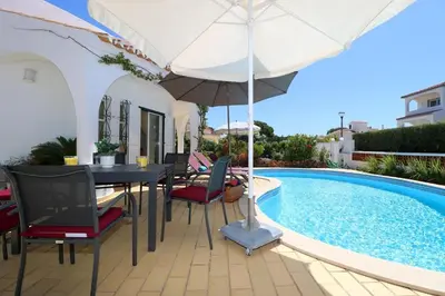 a patio with a table and umbrella next to a swimming pool at Villa Vilamoura, piscina privada in Quarteira