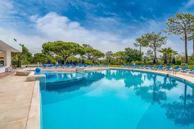 a swimming pool with blue chairs and trees at BmyGuest - Quinta do Lago Cosy Apartment in Quinta do Lago