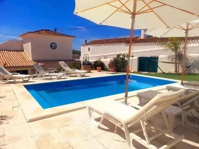 a swimming pool with chairs and an umbrella at Quinta da Calma with pool and BBQ in Boliqueime