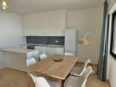 a kitchen with a wooden table and white cabinets at Apartamento moderno na praia com varanda grande in Quarteira