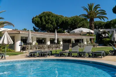 a pool with chairs and umbrellas next to a resort at Luxury Beach House Apartment - Golf & Tennis Court & Pool View in Albufeira