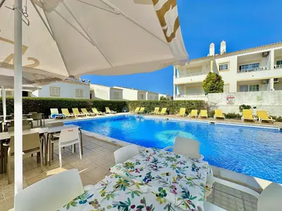 a swimming pool with yellow benches and palm trees at Albufeira Tropical View 2 by Homing in Sesmarias
