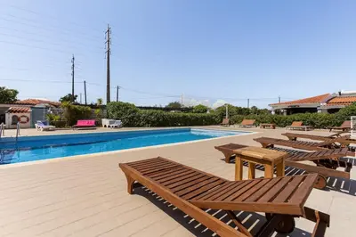 a swimming pool with wooden tables and chairs next to it at Maison A Quinta V2B 7 Personnes in Ferreiras