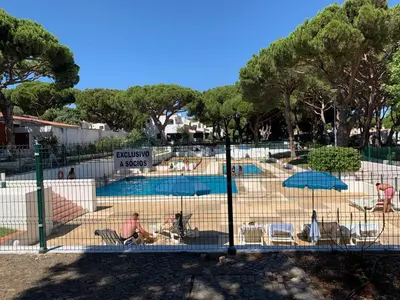 a fence with people sitting in chairs near a pool at Açoteias Falésia Studio Apartment in Olhos de Água