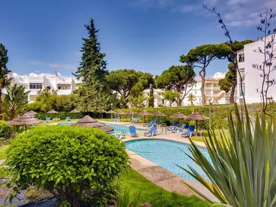 a swimming pool with chairs and umbrellas at a resort at Apartamento Alvaflor com Piscina – Vilamoura in Quarteira