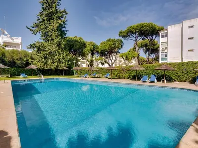 a large blue swimming pool with chairs and umbrellas at Apartamento Alvaflor com Piscina – Vilamoura in Quarteira