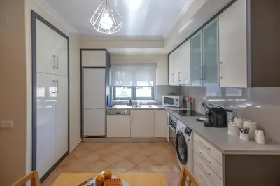 a large kitchen with white cabinets and a table at Moradia Flaj in Olhos de Água