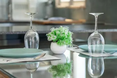 a table with two wine glasses and plates and a plant at Blife Charlya private apartment at Faro beach in Faro